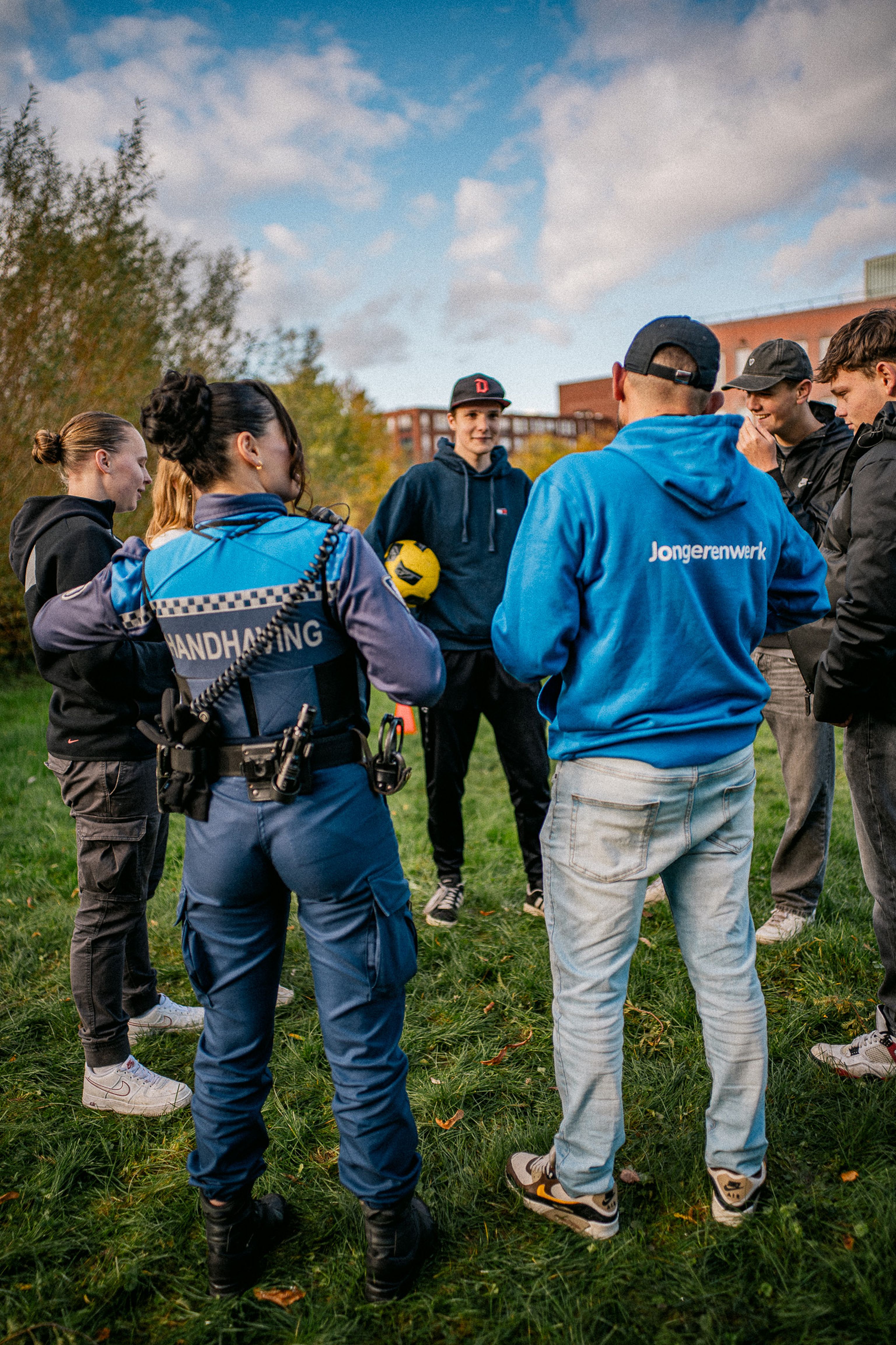 Jongerenwerker en Jeugdboa in gesprek op het grasveld met met jongeren met een voetbal