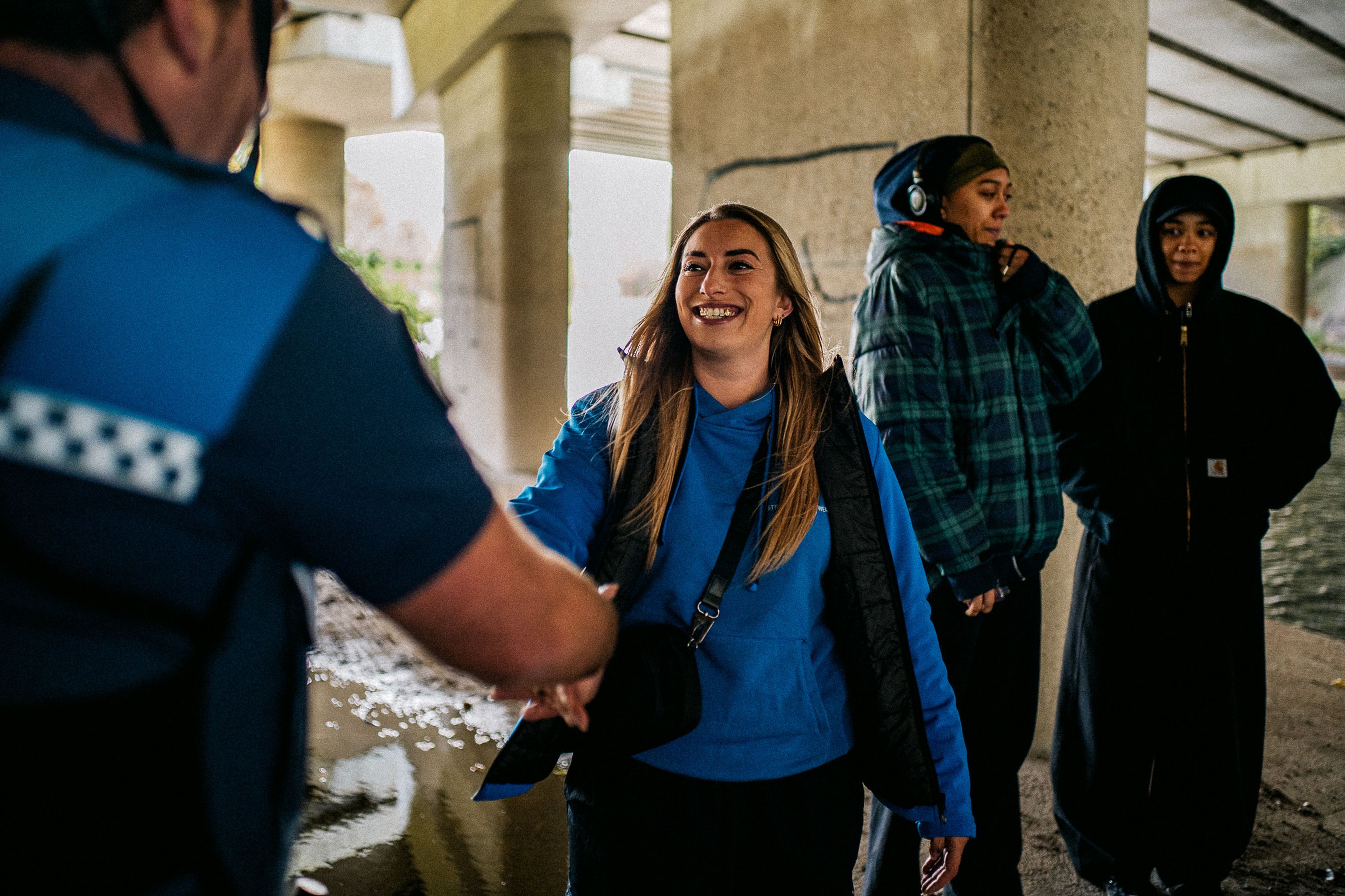 Jongerenwerker geeft hand aan jeugdboa met jeugdgroep op de achtergrond onder viaduct