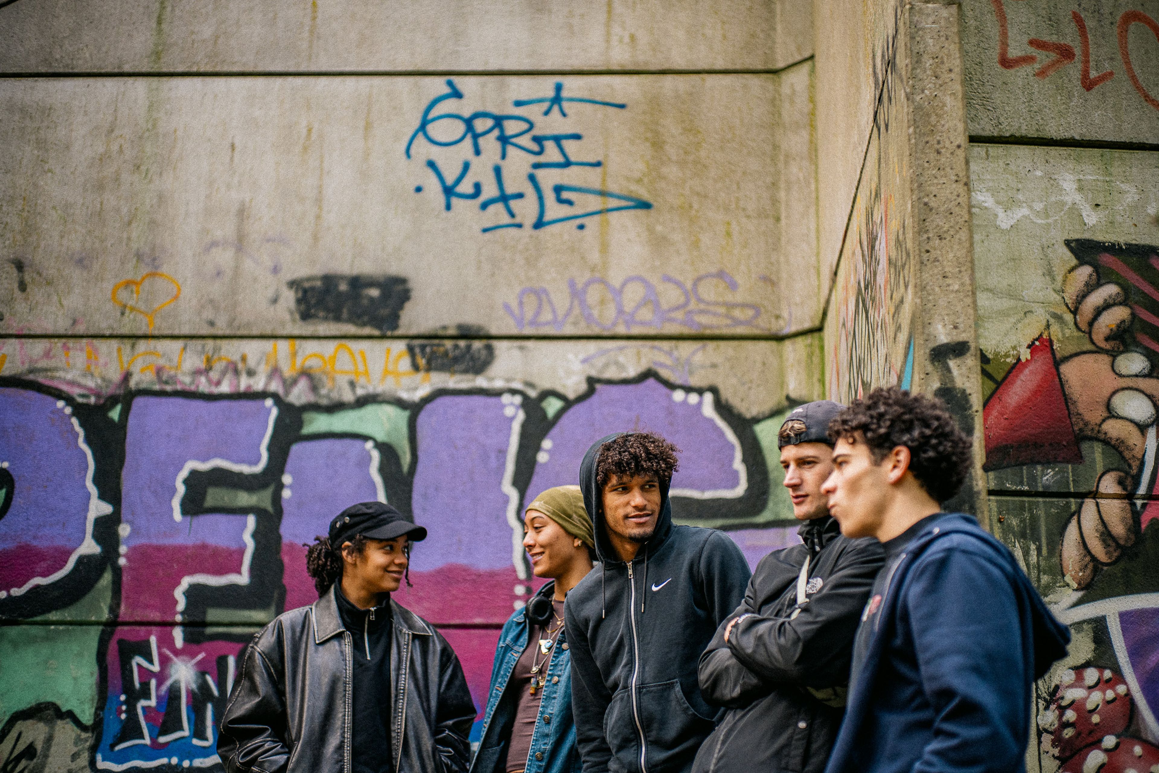 Groep jongeren praat en lacht samen bij een muur met graffiti in de openbare ruimte, als voorbeeld van straatcultuur en jongerenontmoetingen