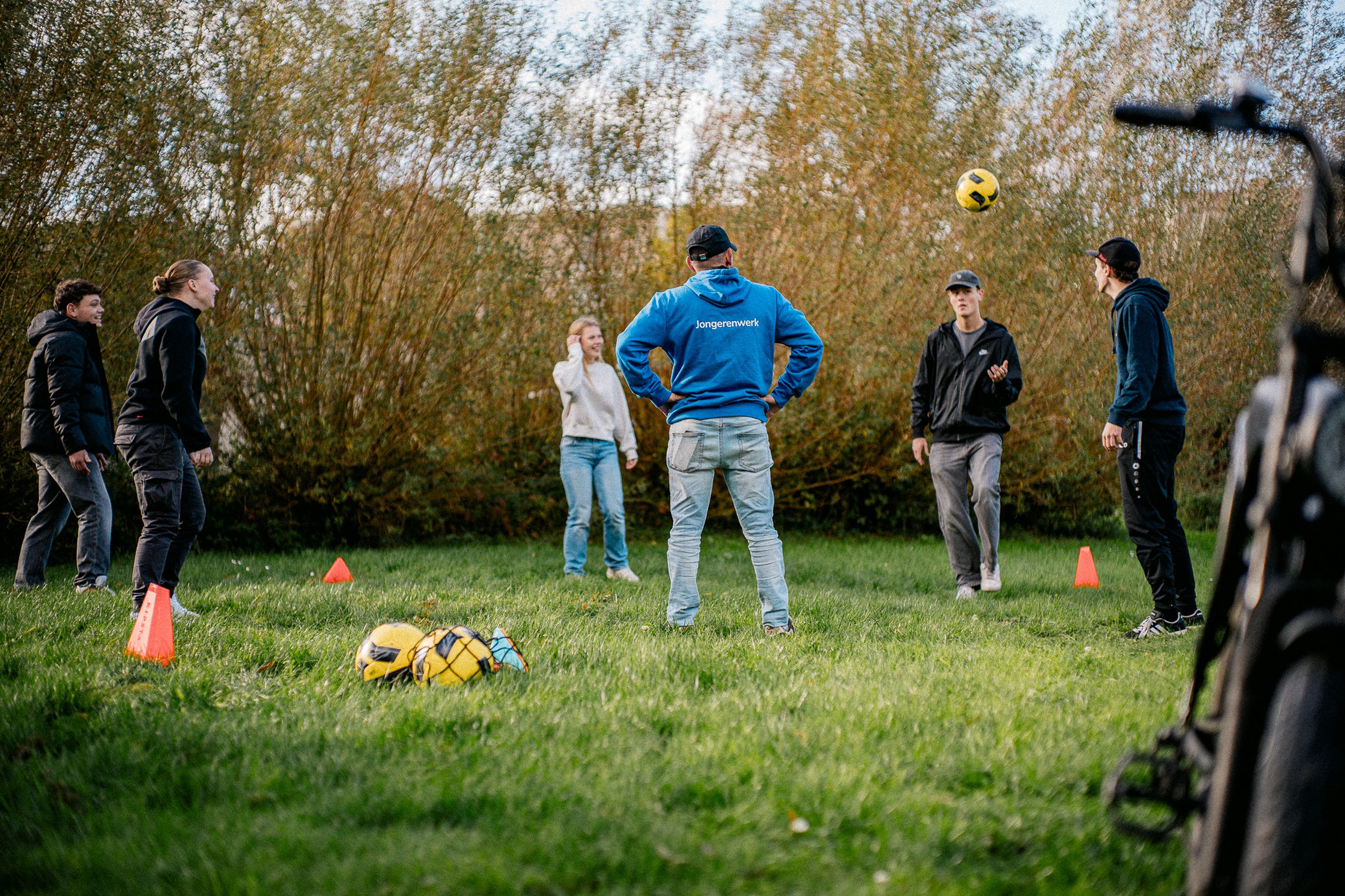 Jongerenwerker van Straatcontact aan het voetballen met jeugdgroep op grasveldje
