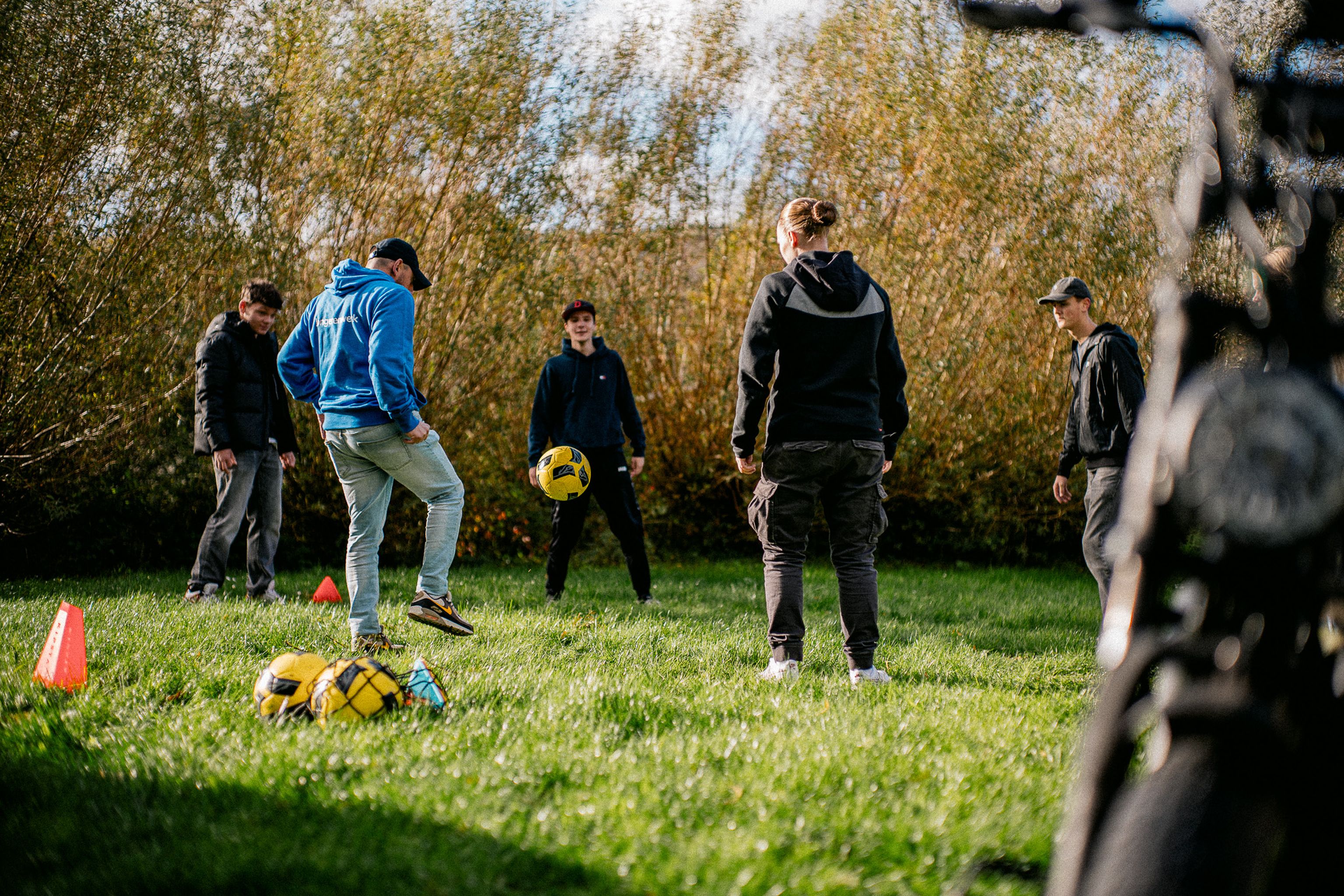 Jongerenwerker aan het voetballen met jongeren op een grasveld